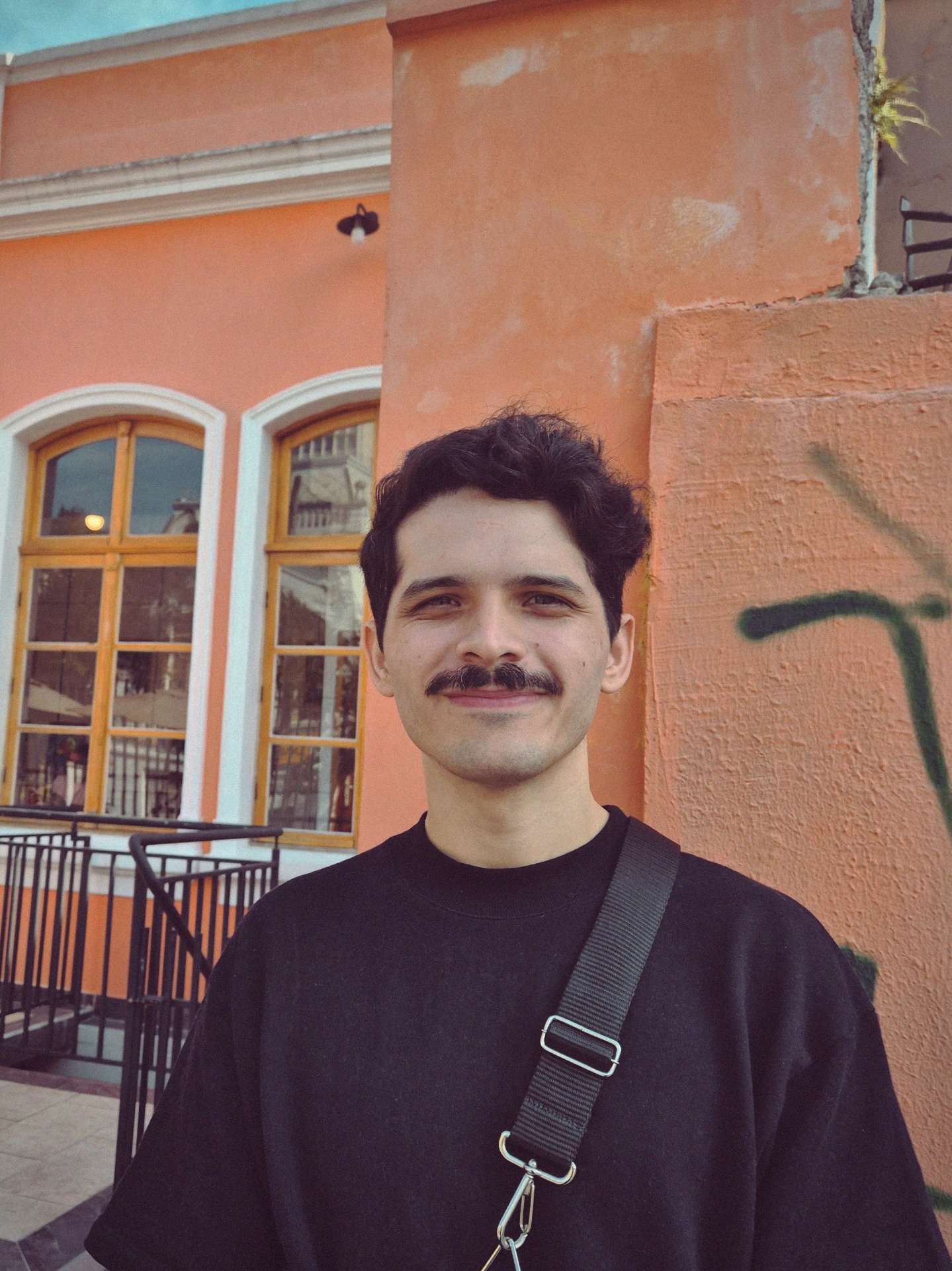 Photography of Facundo Leites. A 30 years old male, with short black hair and a moustache wearing a black oversized t-shirt.